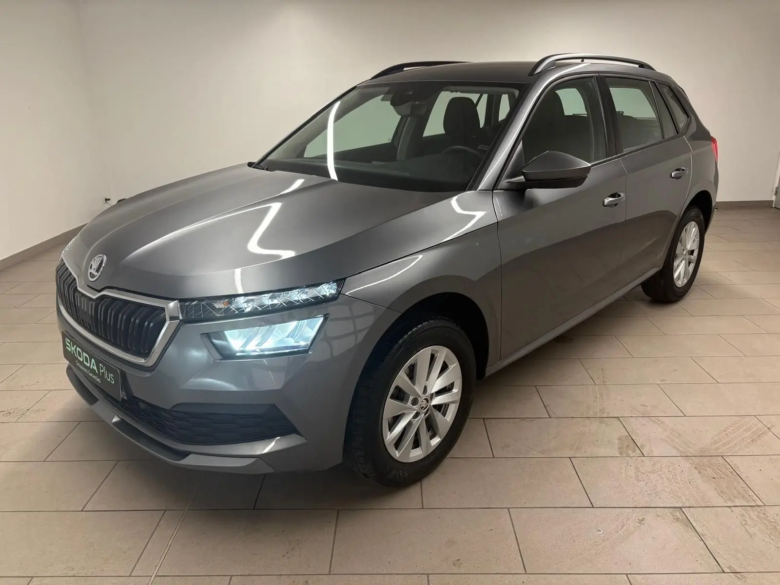 SKODA KAMIQ 1.0 TSI 2023 gris graphite, vue 3/4 avant droit avec phares allumés en intérieur.
