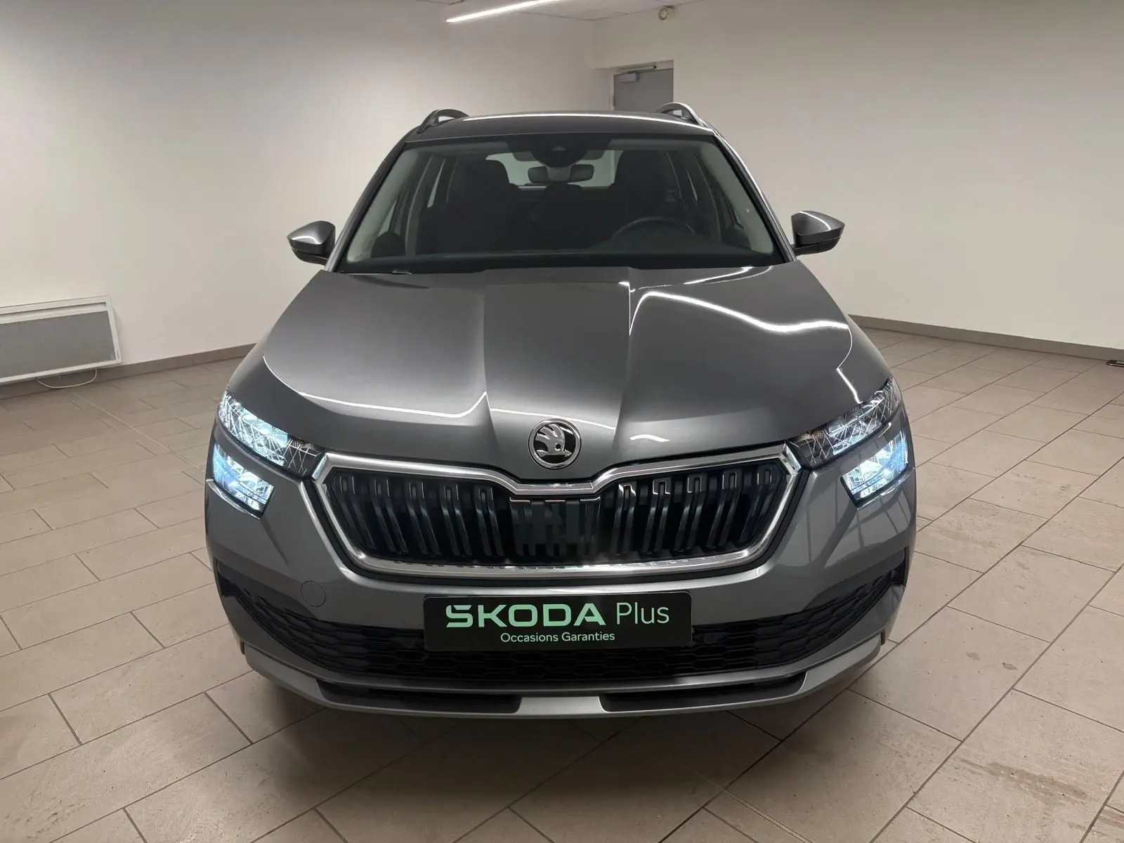 Vue avant d'un Skoda Kamiq 2023 gris graphite avec calandre noire et phares allumés en intérieur.