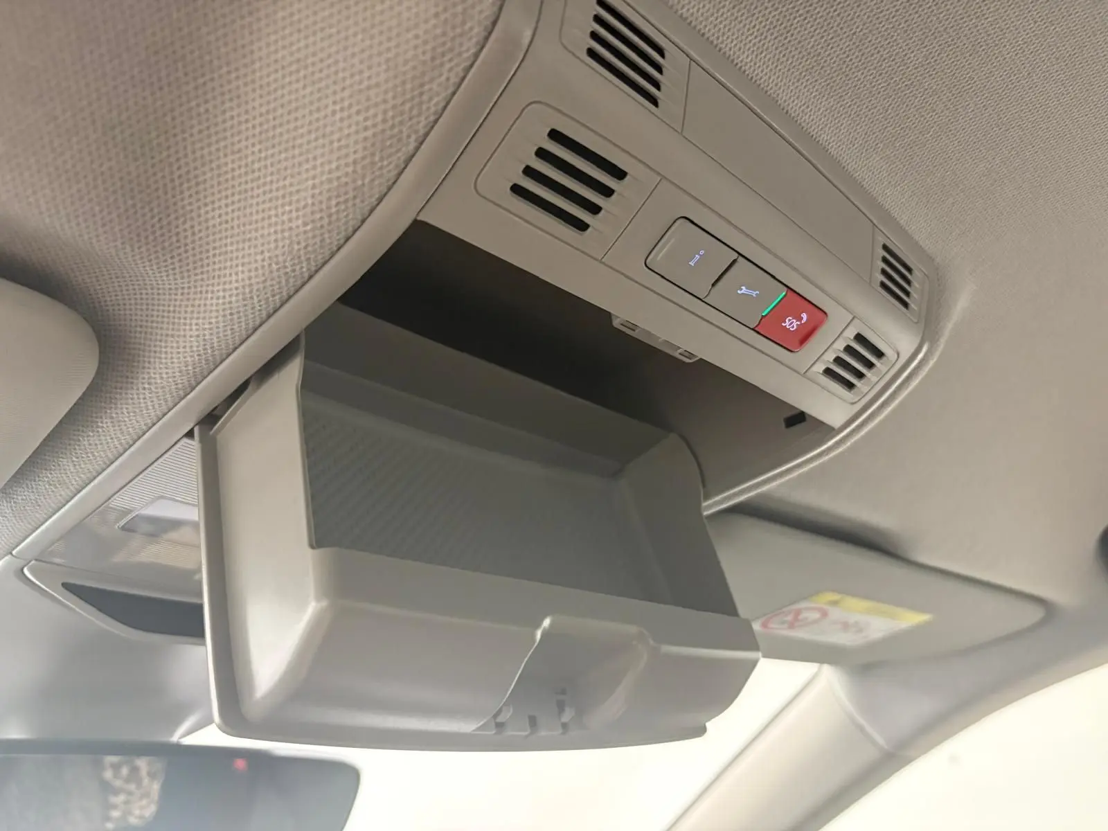 Vue intérieure en plongée du compartiment de rangement ouvert au plafond du Skoda Kamiq 2023 gris graphite, avec commandes SOS visibles.
