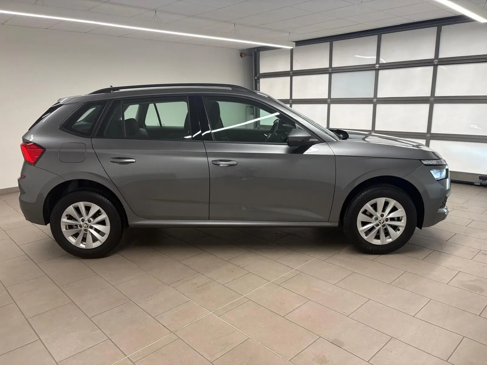 Vue de profil côté gauche d'un Skoda Kamiq 2023 gris graphite métallisé avec jantes alliage en intérieur lumineux.