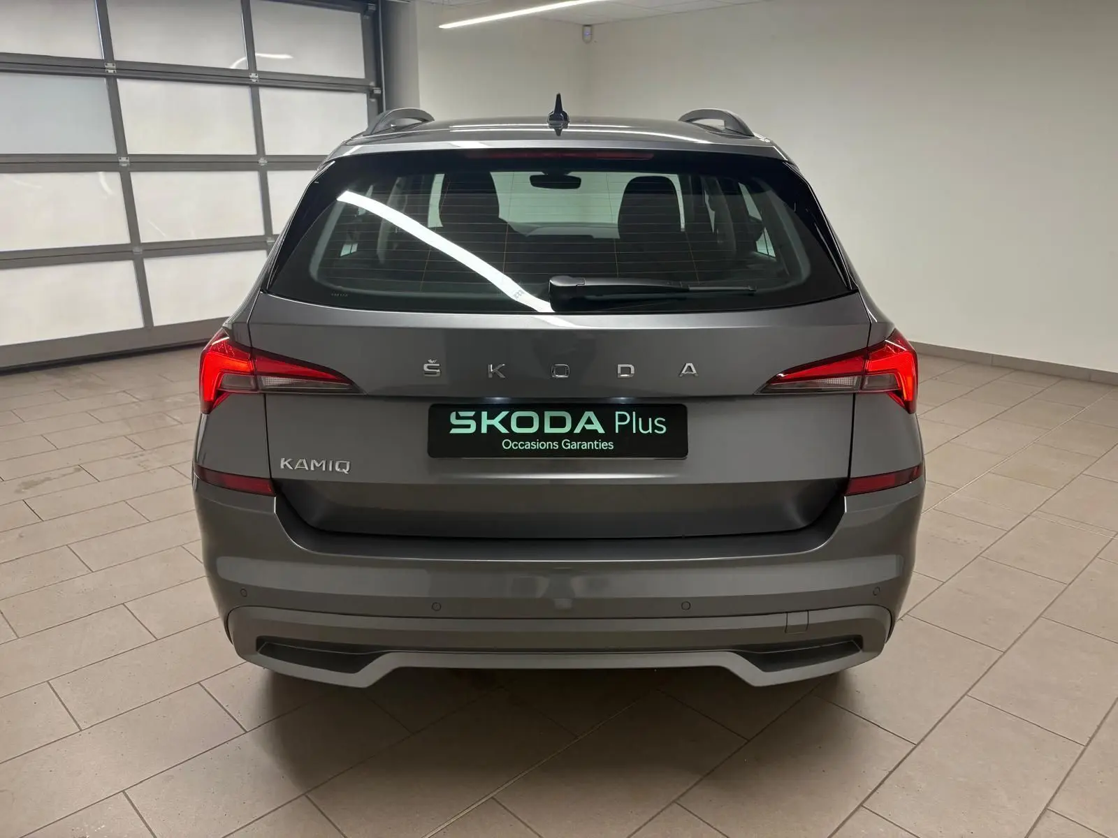 Vue arrière d'un Skoda Kamiq 2023 gris graphite avec feux LED et logo ŠKODA bien visibles dans un garage.