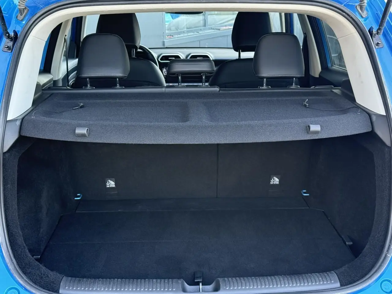 Coffre ouvert d’un MG Motor ZS 1.5 Hybrid+ 197 Luxury bleu Como, avec cache-bagages et sièges arrière noirs visibles.