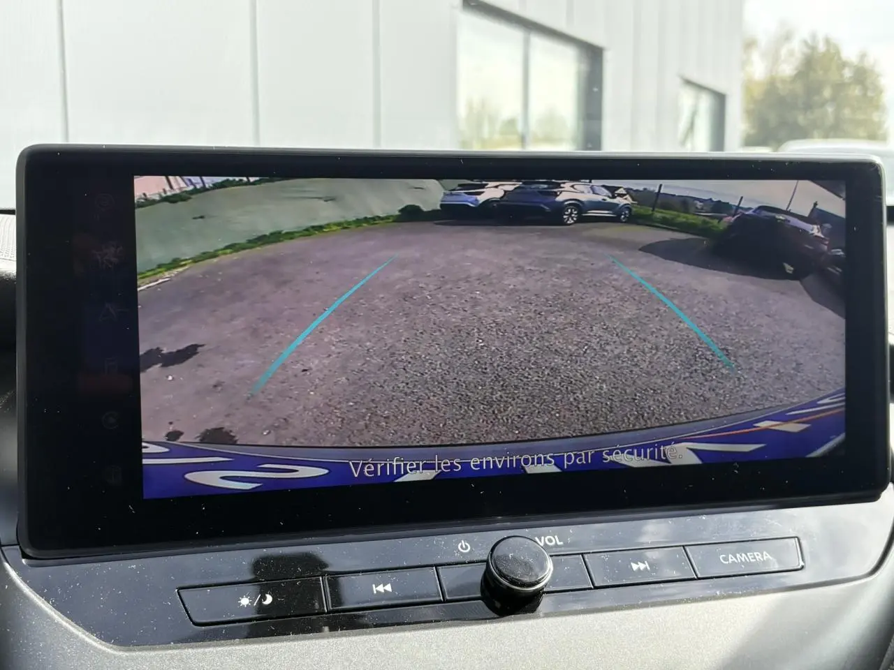 Vue de l'écran de caméra de recul affichant un parking avec plusieurs véhicules, dans un Nissan Juke gris Ceramic.