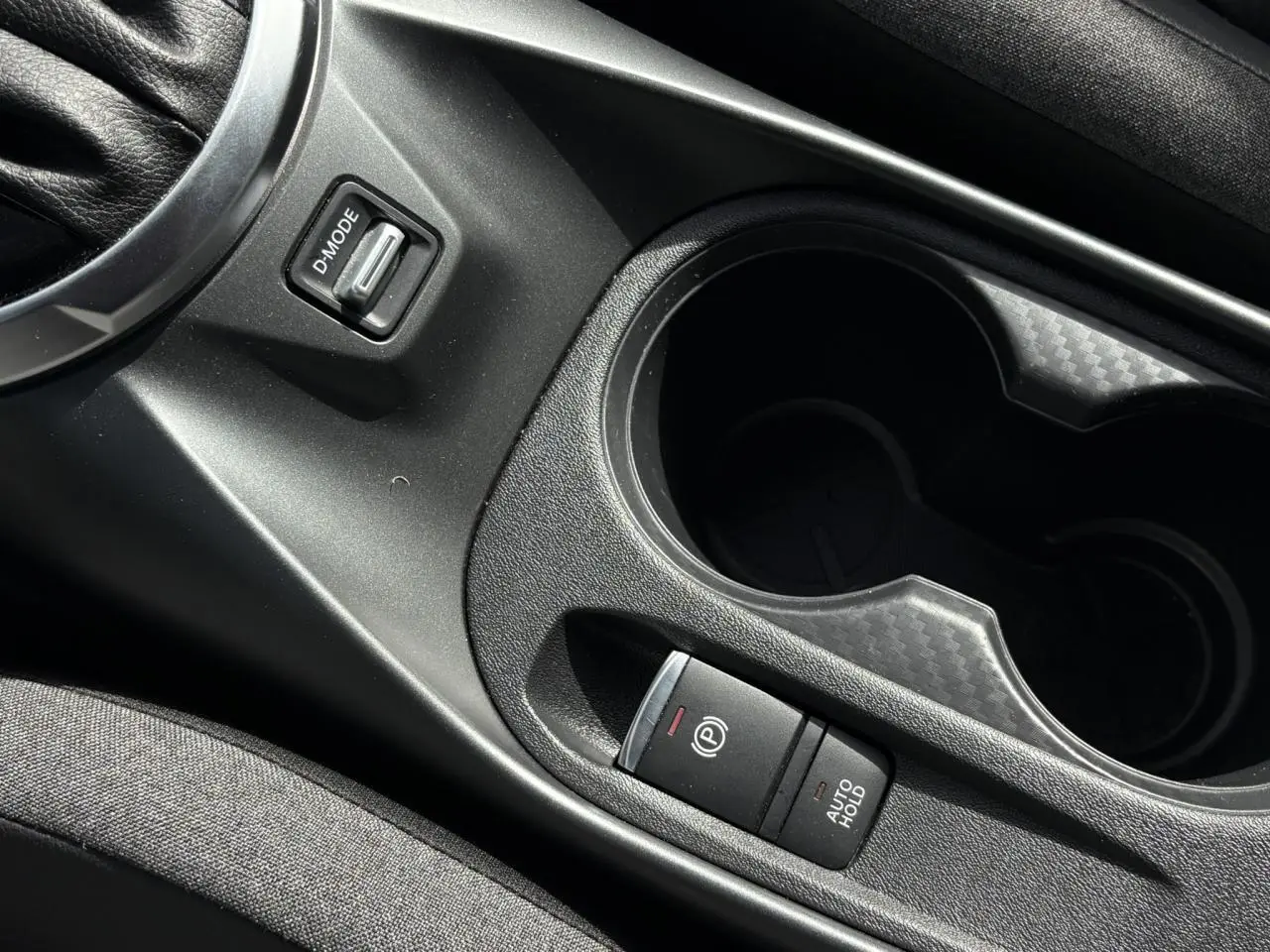 Gros plan sur la console centrale noire du Nissan Juke 2025, avec frein à main électrique et porte-gobelets.