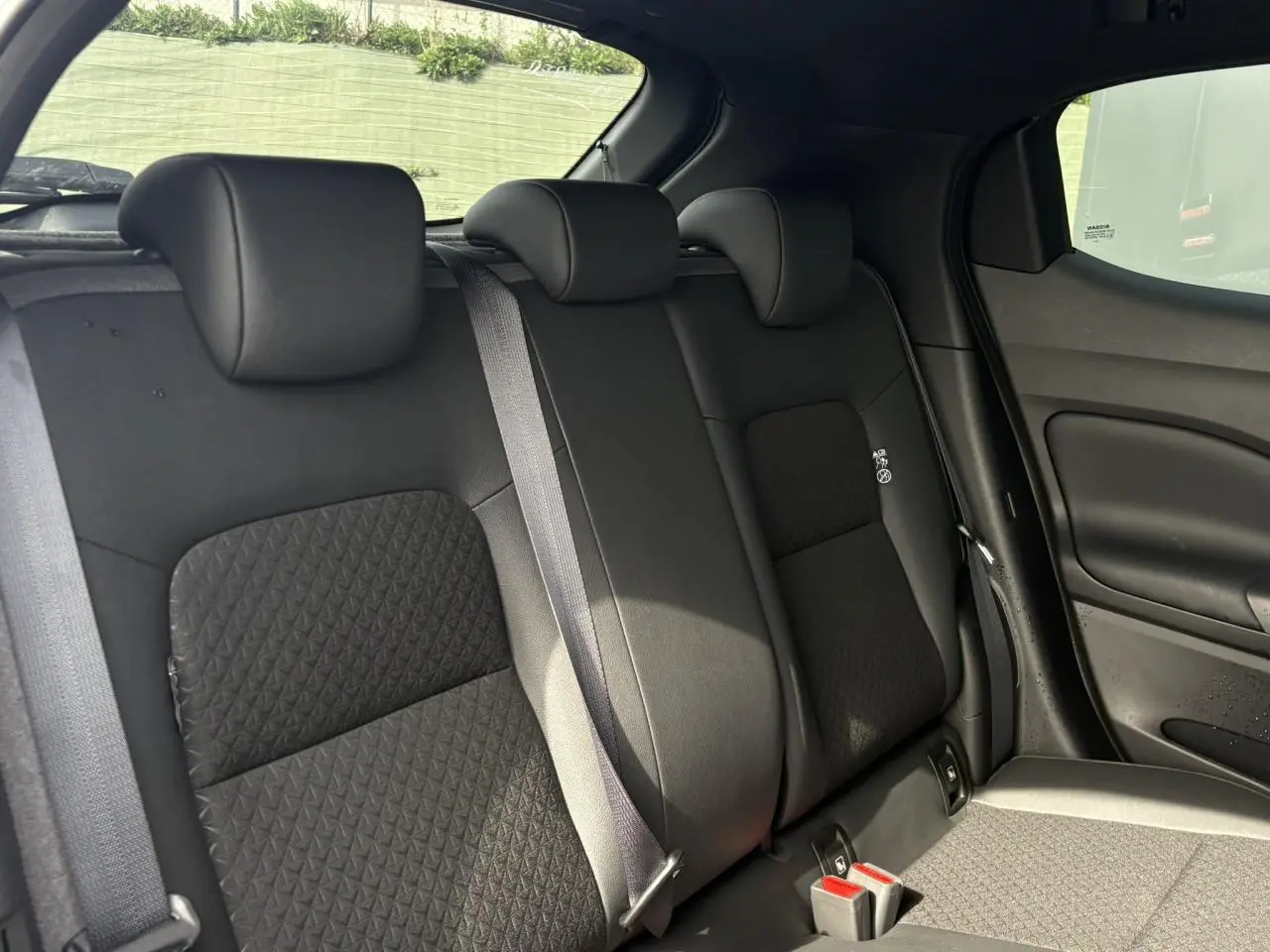 Vue intérieure du siège arrière droit du Nissan Juke 2025, avec sellerie noire et ceintures grises visibles.