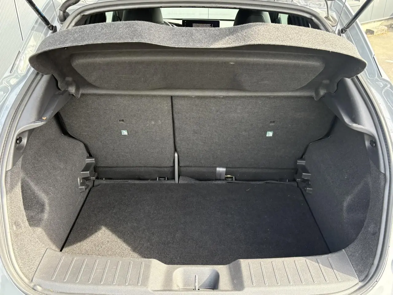 Coffre ouvert du Nissan Juke gris Ceramic 2025, vue arrière montrant le plancher de coffre modulable et l'espace de rangement.