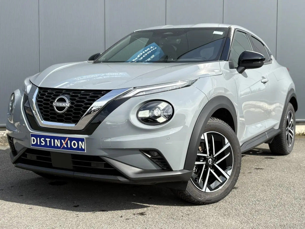 Nissan Juke gris Ceramic en 3/4 avant droit, avec calandre chromée et jantes alliage noires et argentées.