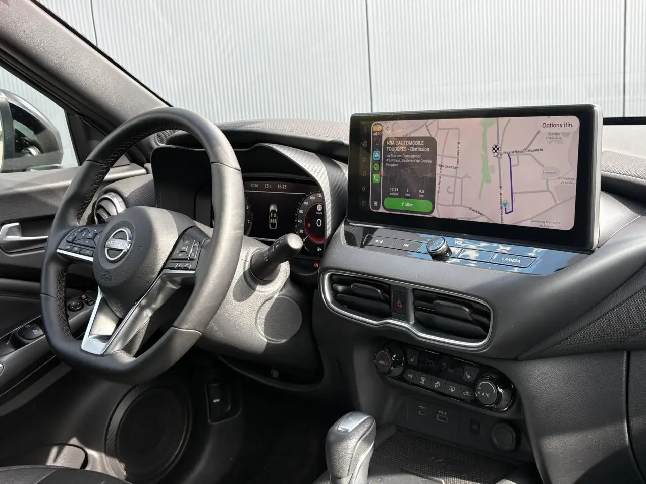 Vue intérieure côté conducteur du Nissan Juke 2025, tableau de bord noir avec écran tactile GPS et volant multifonction.