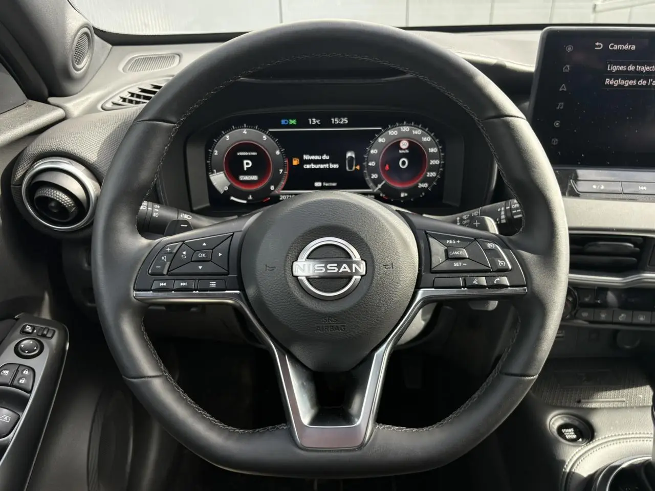 Vue intérieure centrée sur le volant noir du Nissan Juke 2025 avec tableau de bord digital et écran tactile.