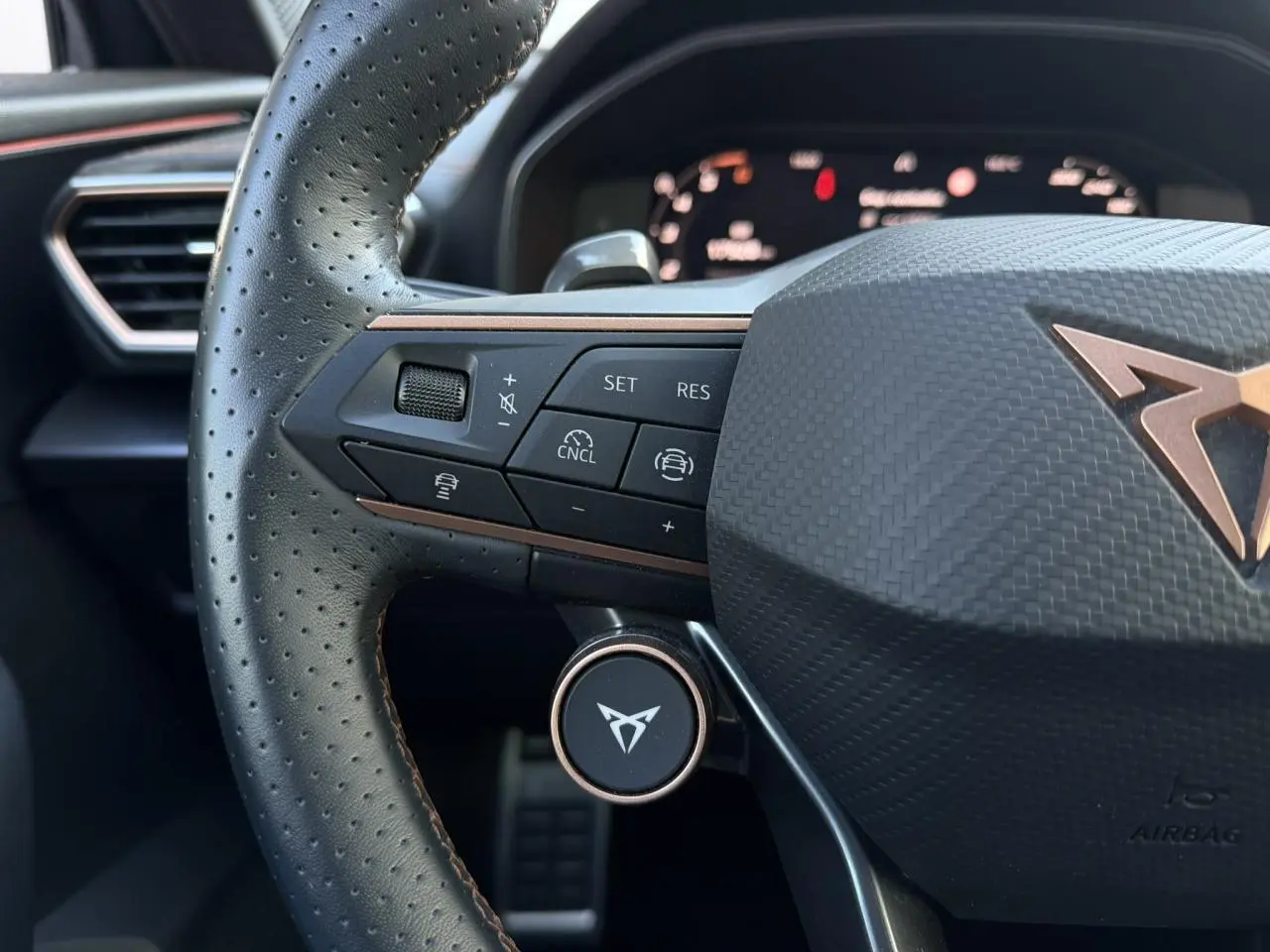 Gros plan sur le volant cuir perforé noir du CUPRA Formentor 2025 avec commandes multifonctions et logo cuivre central.