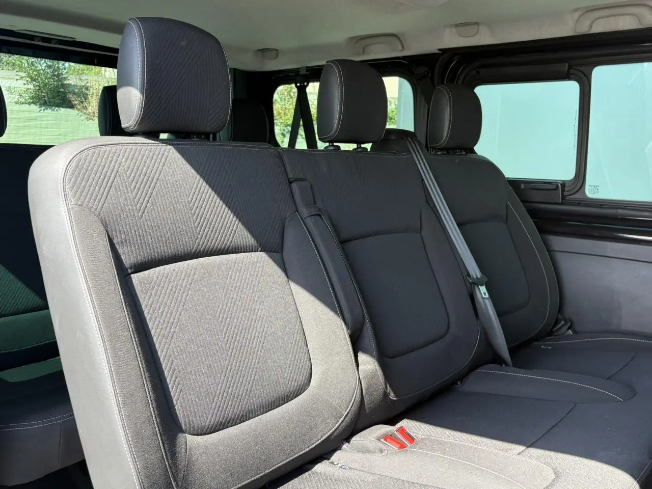 Vue intérieure sur la deuxième rangée de sièges noirs du Nissan Primastar Combi 2025, avec ceintures et appuie-têtes visibles.
