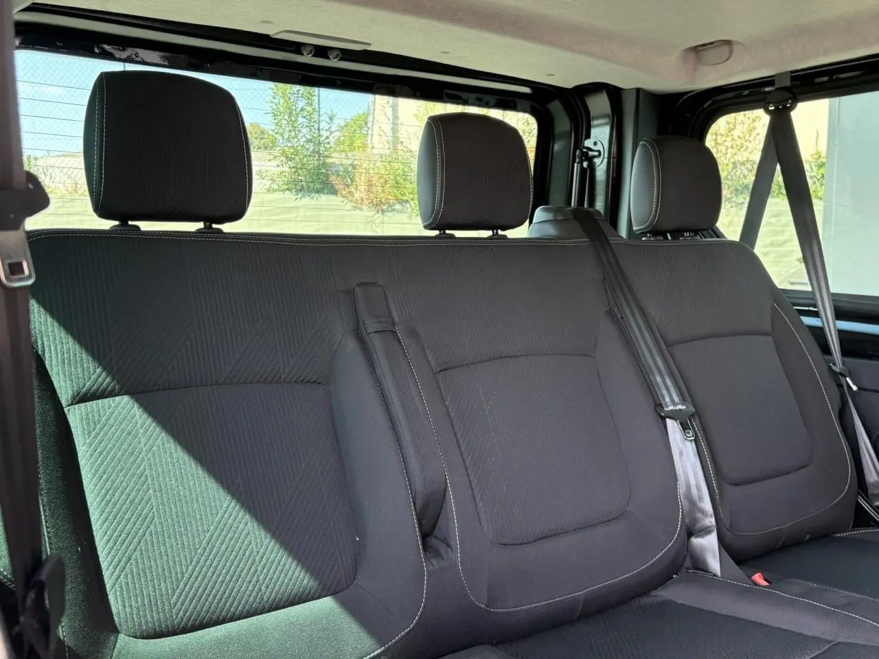 Vue intérieure sur la banquette arrière noire du Nissan Primastar Combi 2025 avec ceintures de sécurité visibles.