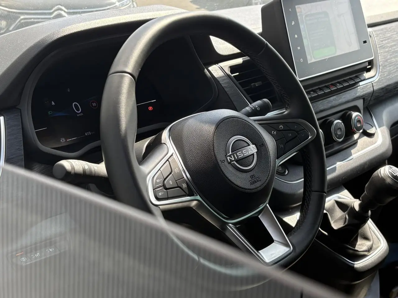 Vue rapprochée du volant et tableau de bord noir du Nissan Primastar Combi avec levier de vitesses manuel et écran tactile.