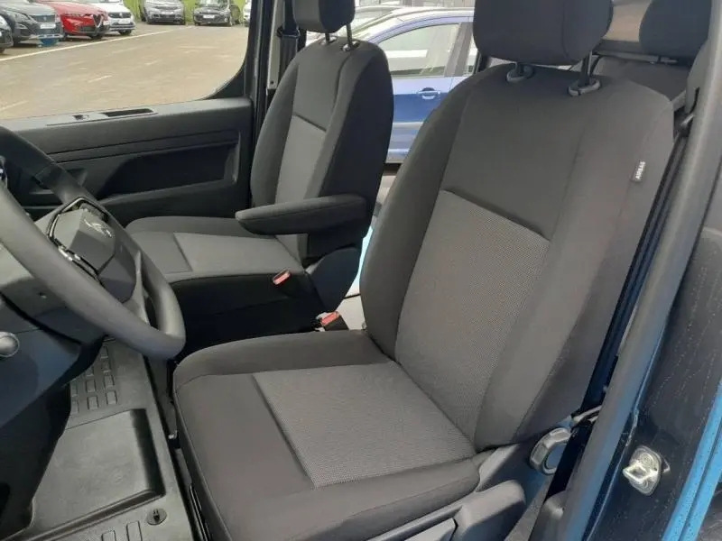 Vue intérieure côté conducteur du Citroën Jumpy gris Titane 2025, sièges tissu bi-ton noir et gris avec accoudoir.