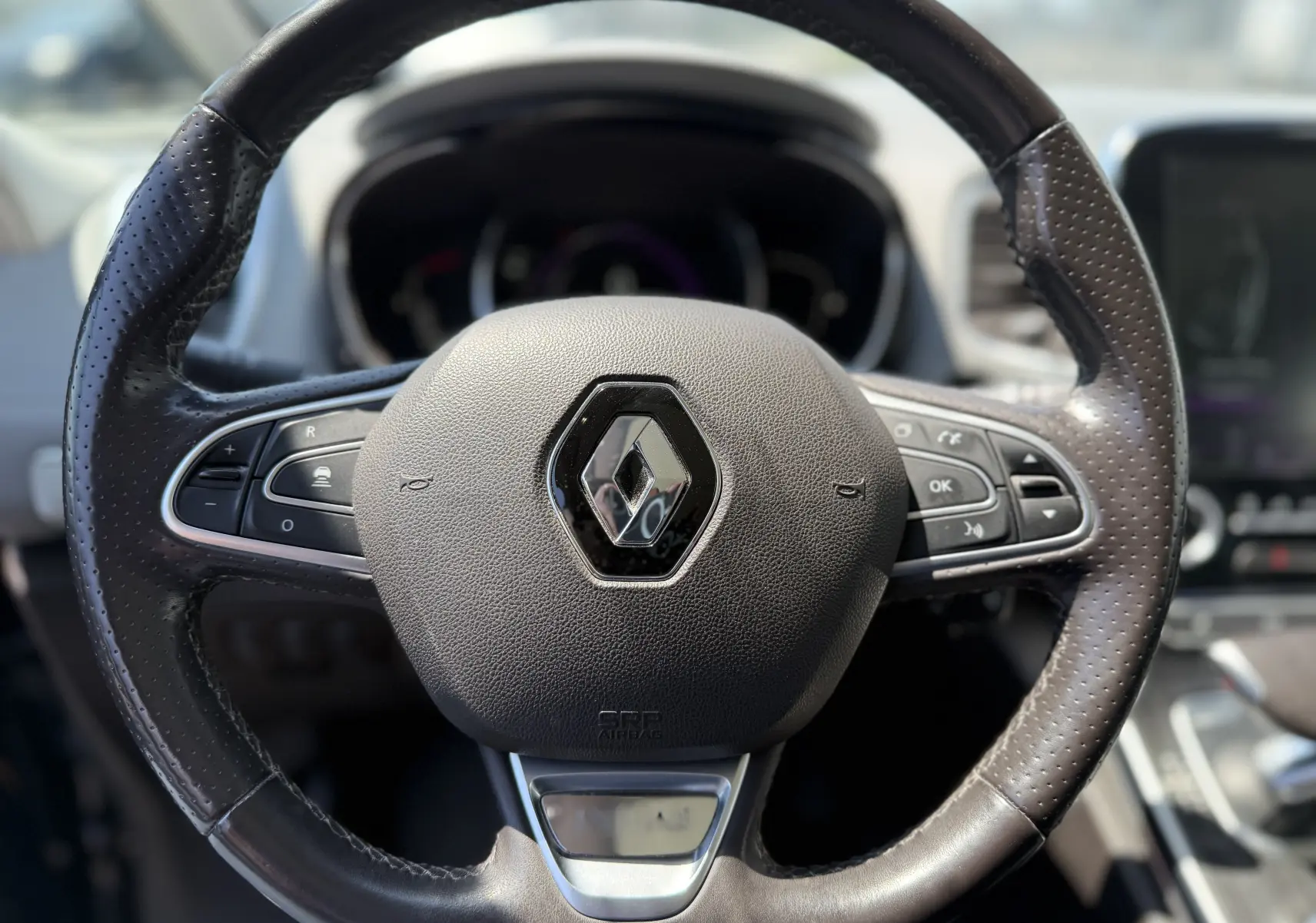 Gros plan sur le volant en cuir noir du Renault Espace V, avec commandes intégrées et logo central brillant.