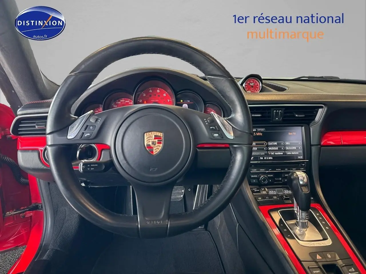 Vue intérieure centrée sur le volant cuir noir et le tableau de bord rouge de la Porsche 911 Carrera 4 PDK rouge.