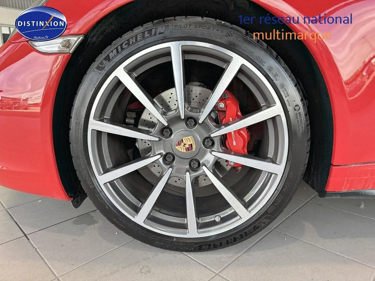 Gros plan sur la jante alu grise et l'étrier de frein rouge d'une Porsche 911 Carrera 4 rouge côté avant droit.