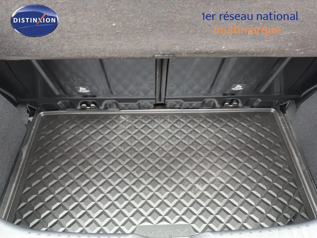 Vue plongeante sur le coffre ouvert d'une Toyota Aygo X noire, mettant en valeur le tapis de coffre texturé.