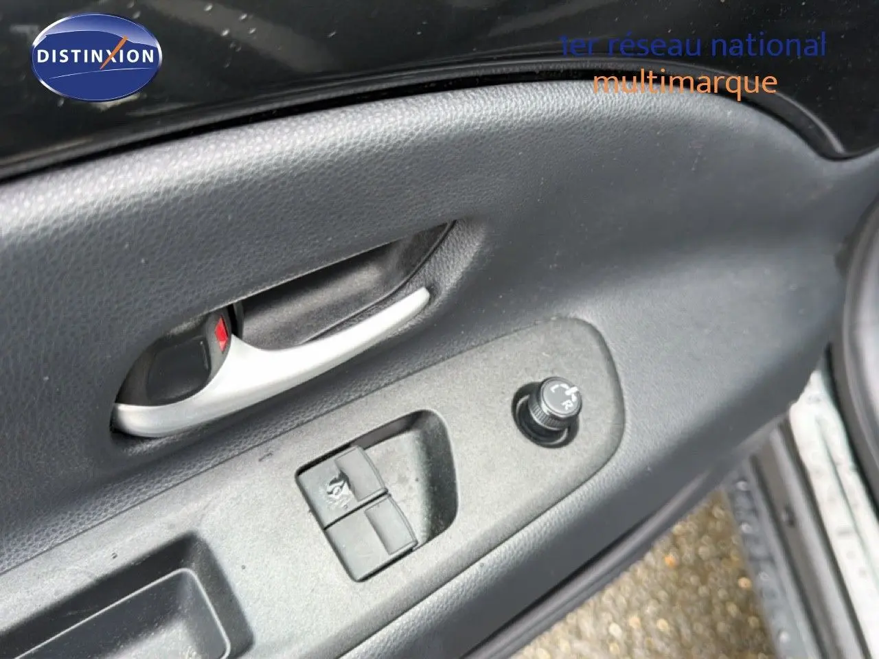 Détail de la porte côté gauche de la Toyota Aygo X noire 2025, montrant la poignée intérieure et les commandes des vitres et rétroviseurs.