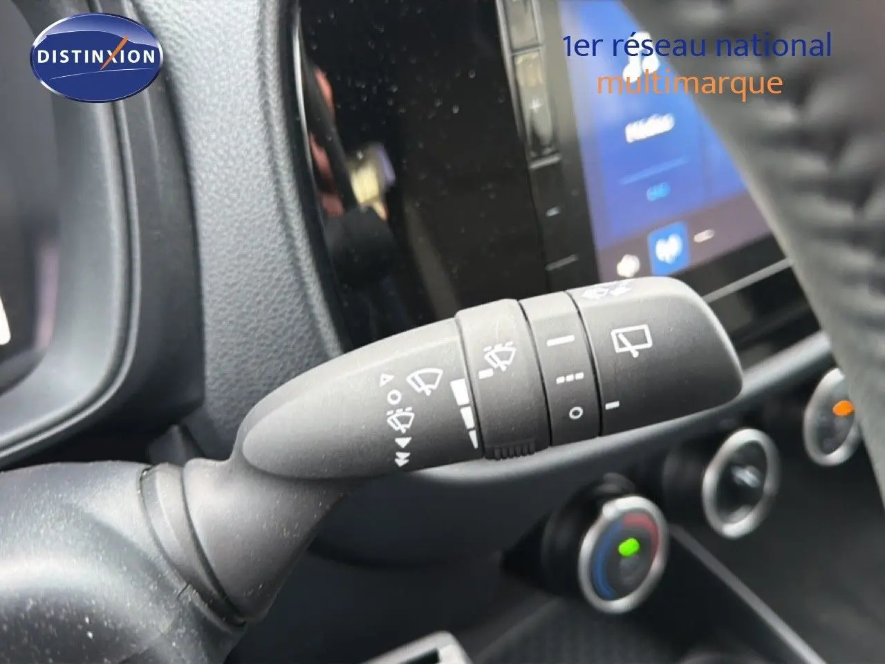 Gros plan sur la commande d’essuie-glace dans l’habitacle noir de la Toyota Aygo X 2025, avec tableau de bord et écran tactile en arrière-plan.