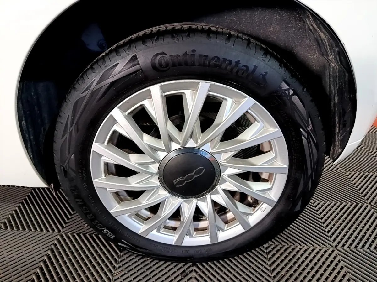 Gros plan sur la roue avant droite d'une FIAT 500 blanche, avec jante argentée au design étoilé et pneu Continental.