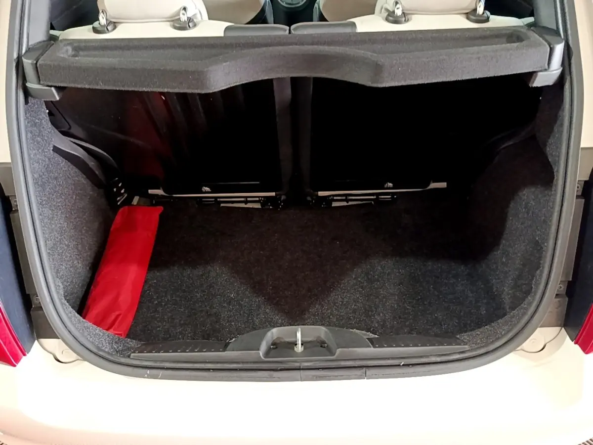 Coffre ouvert vu de l'arrière d'une Fiat 500 blanche avec intérieur noir et sac rouge sur le côté gauche.