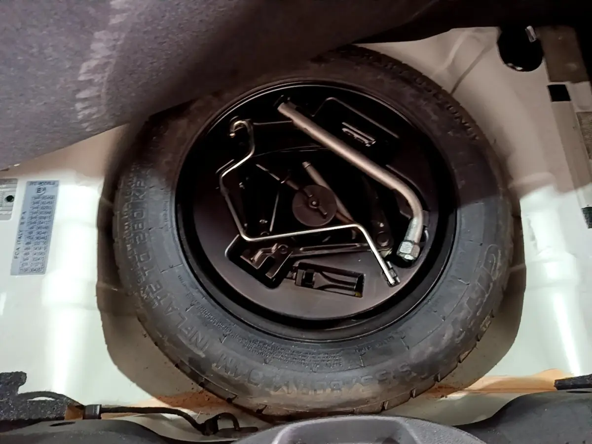 Vue rapprochée de la roue de secours et des outils dans le coffre d’une Fiat 500 blanche hybride 2021.