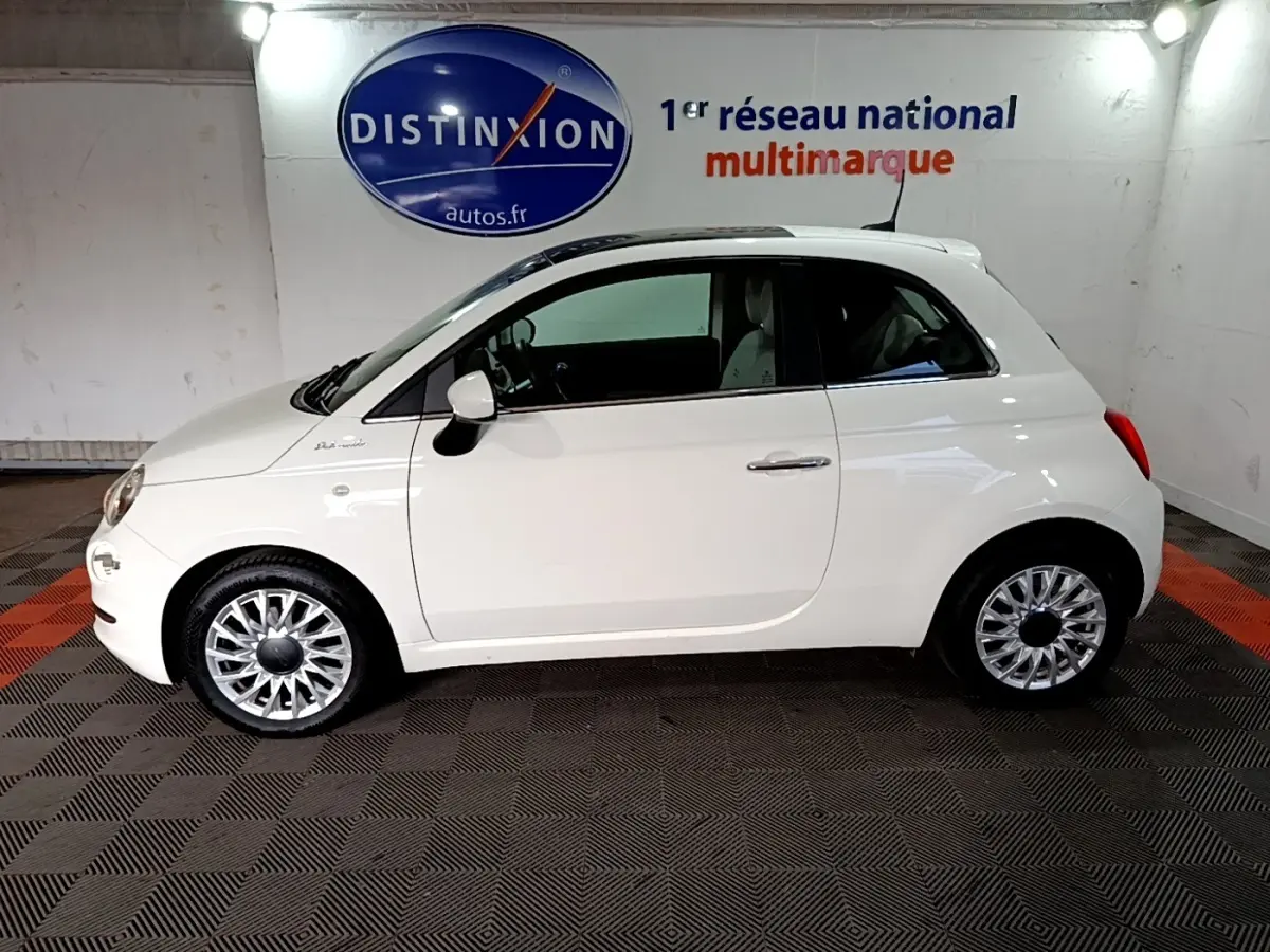 Profil côté gauche d'une Fiat 500 blanche Hybrid 2021, avec jantes argentées et toit blanc dans un showroom.