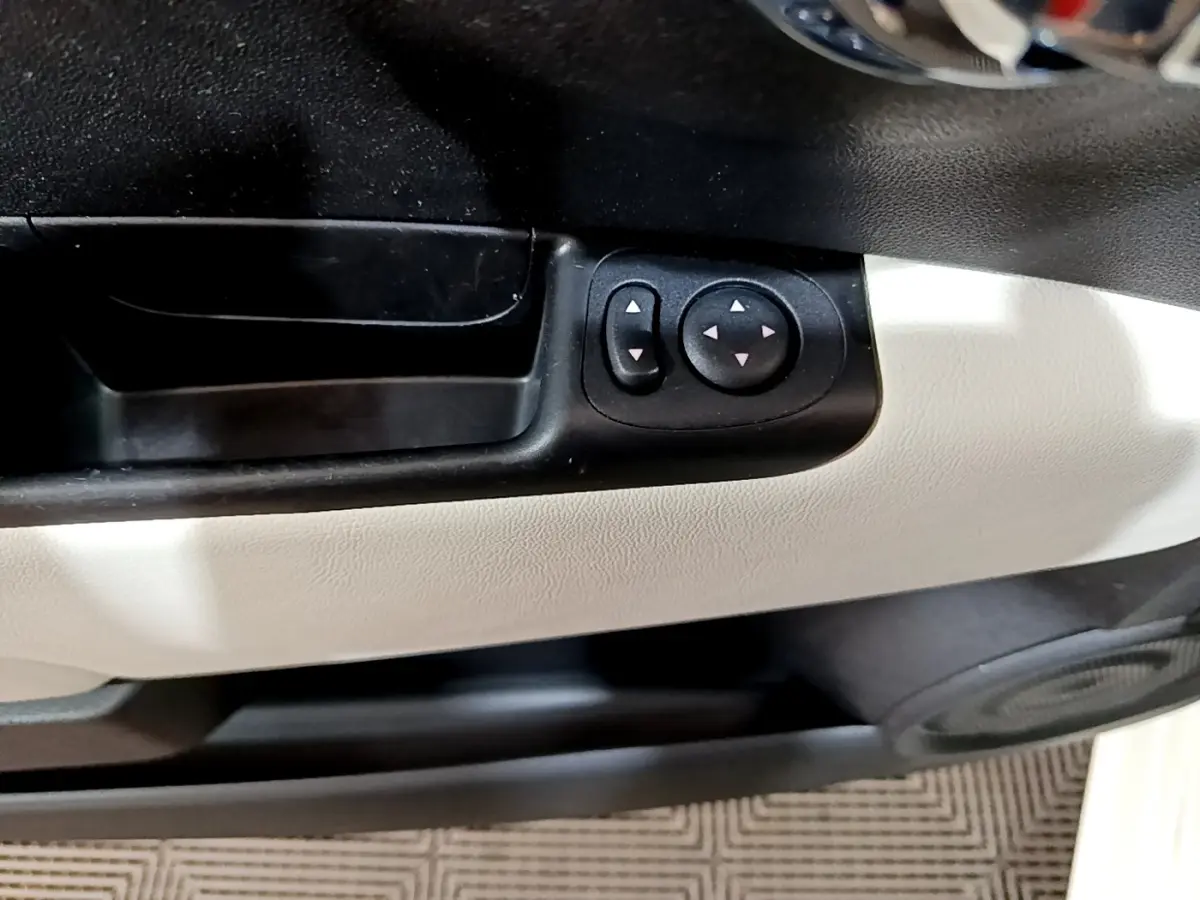 Gros plan sur les commandes de réglage des rétroviseurs noirs sur la porte intérieure blanche d'une Fiat 500 Hybrid 2021.