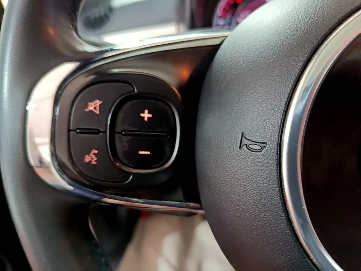 Gros plan sur les commandes gauche du volant cuir de la Fiat 500 blanche Hybrid 2021, avec boutons de volume et téléphone.