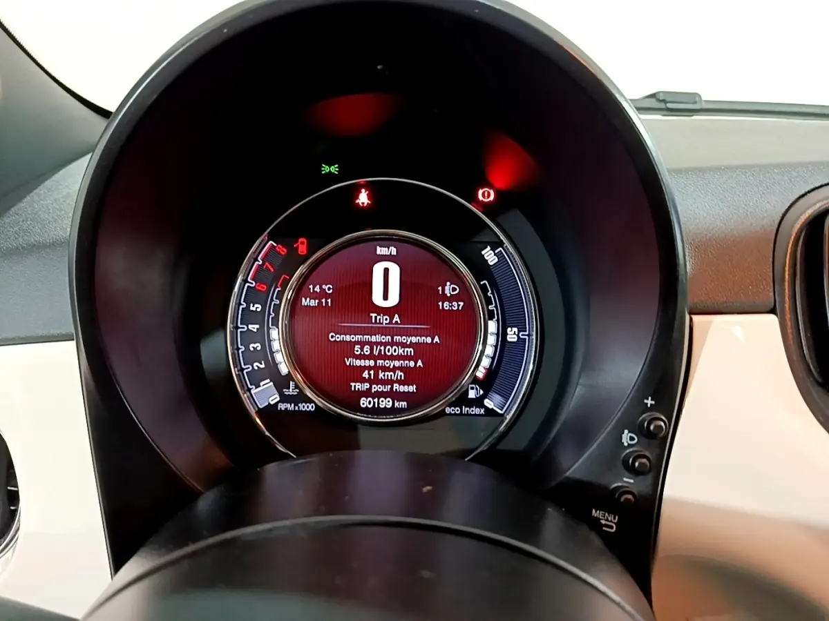 Vue rapprochée du tableau de bord numérique circulaire de la Fiat 500 blanche, affichant la consommation et la vitesse.