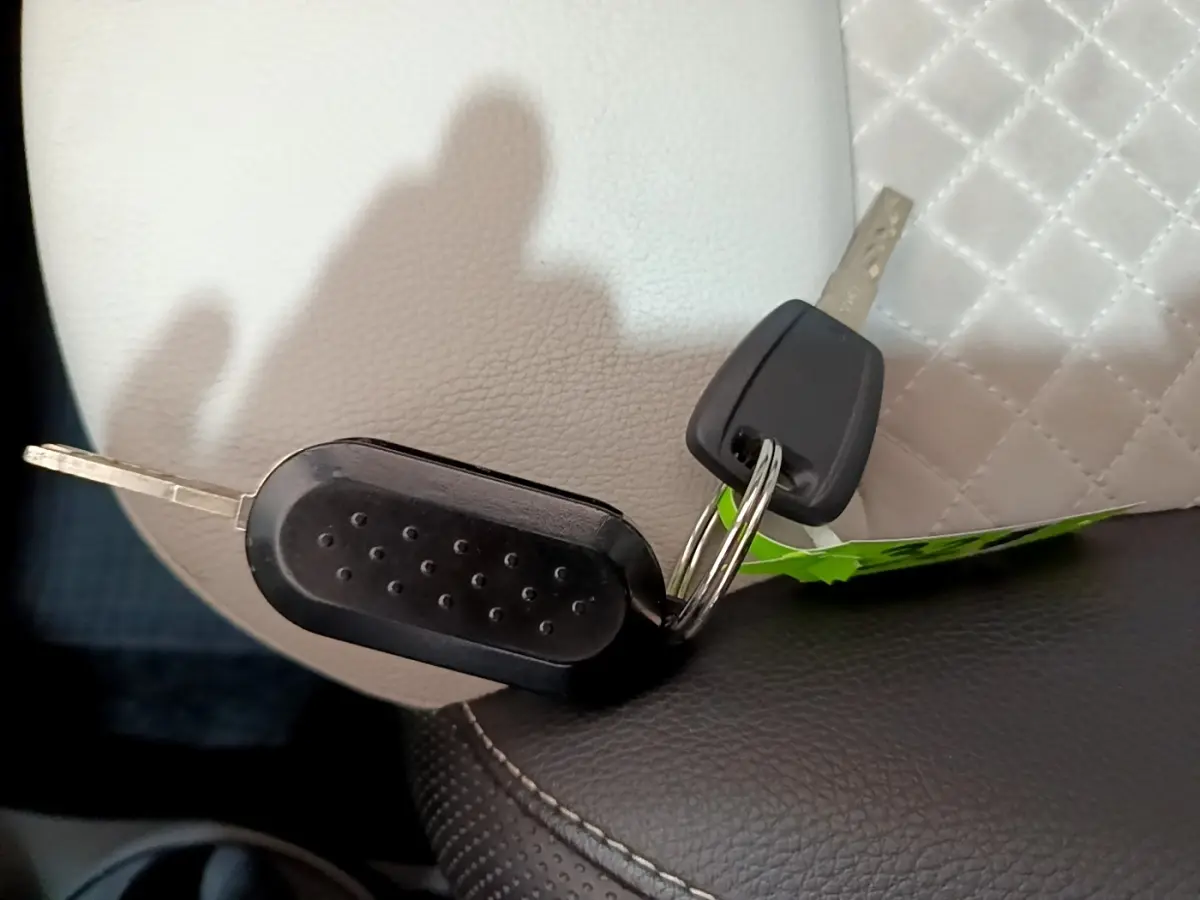 Gros plan sur deux clés noires posées sur un siège en cuir blanc et noir, sans vue du véhicule.