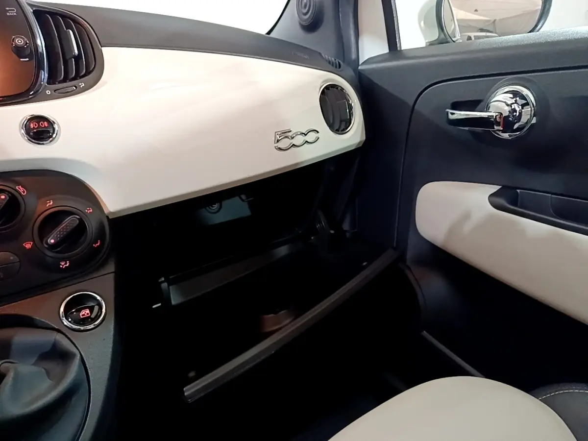 Vue intérieure côté passager de la FIAT 500 blanche, tableau de bord avec logo 500 et boîte à gants ouverte.