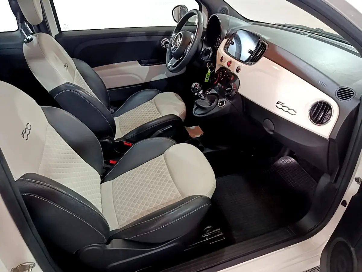 Vue intérieure côté conducteur de la Fiat 500 Hybrid blanche, avec sièges bicolores et tableau de bord épuré.