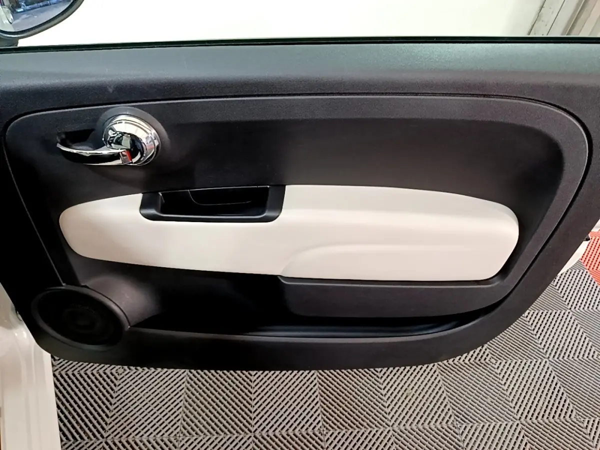 Vue intérieure du panneau de porte côté conducteur de la FIAT 500 blanc avec poignée chromée et insert beige.