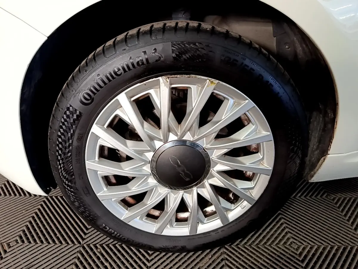 Gros plan sur la roue avant droite blanche d'une Fiat 500 Hybrid avec jante argentée au design étoilé.