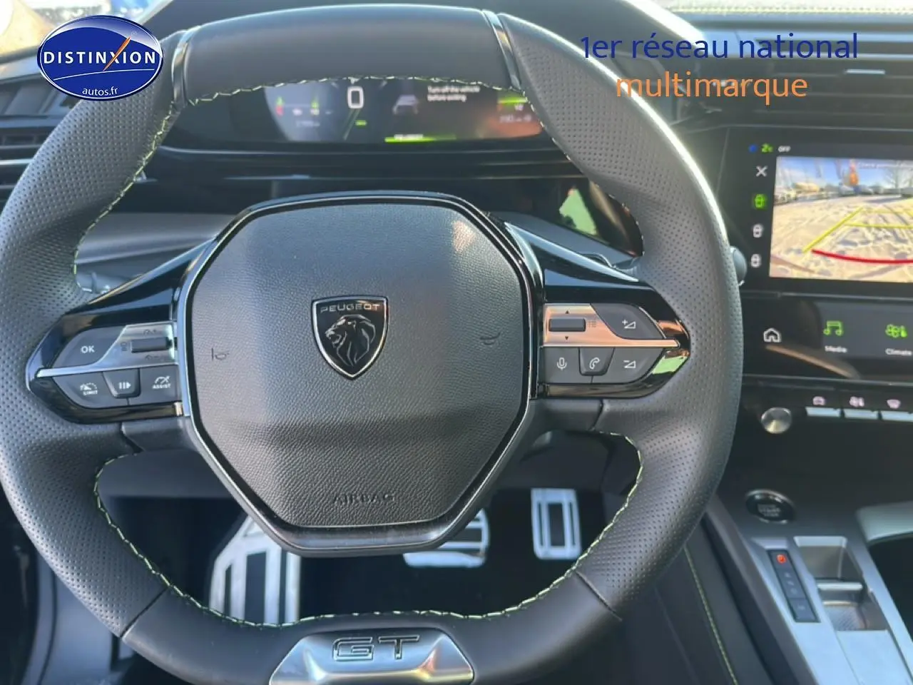 Vue rapprochée du volant cuir noir avec logo Peugeot et commandes intégrées, tableau de bord et écran tactile visibles.