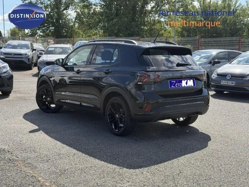 Volkswagen T-Cross 1.0 TSI R-Line noir nacré en 3/4 arrière droit, avec jantes noires et barres de toit visibles.
