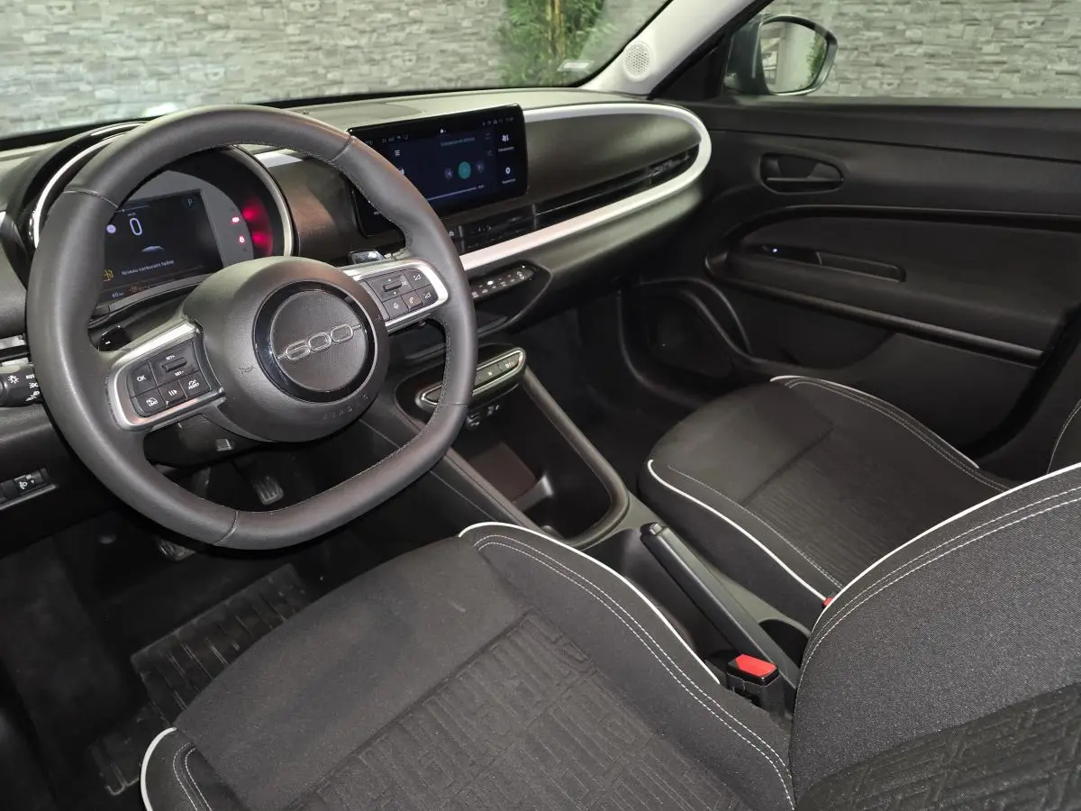Vue intérieure côté conducteur de la Fiat 600 2024, volant avec logo 600 et tableau de bord numérique moderne.