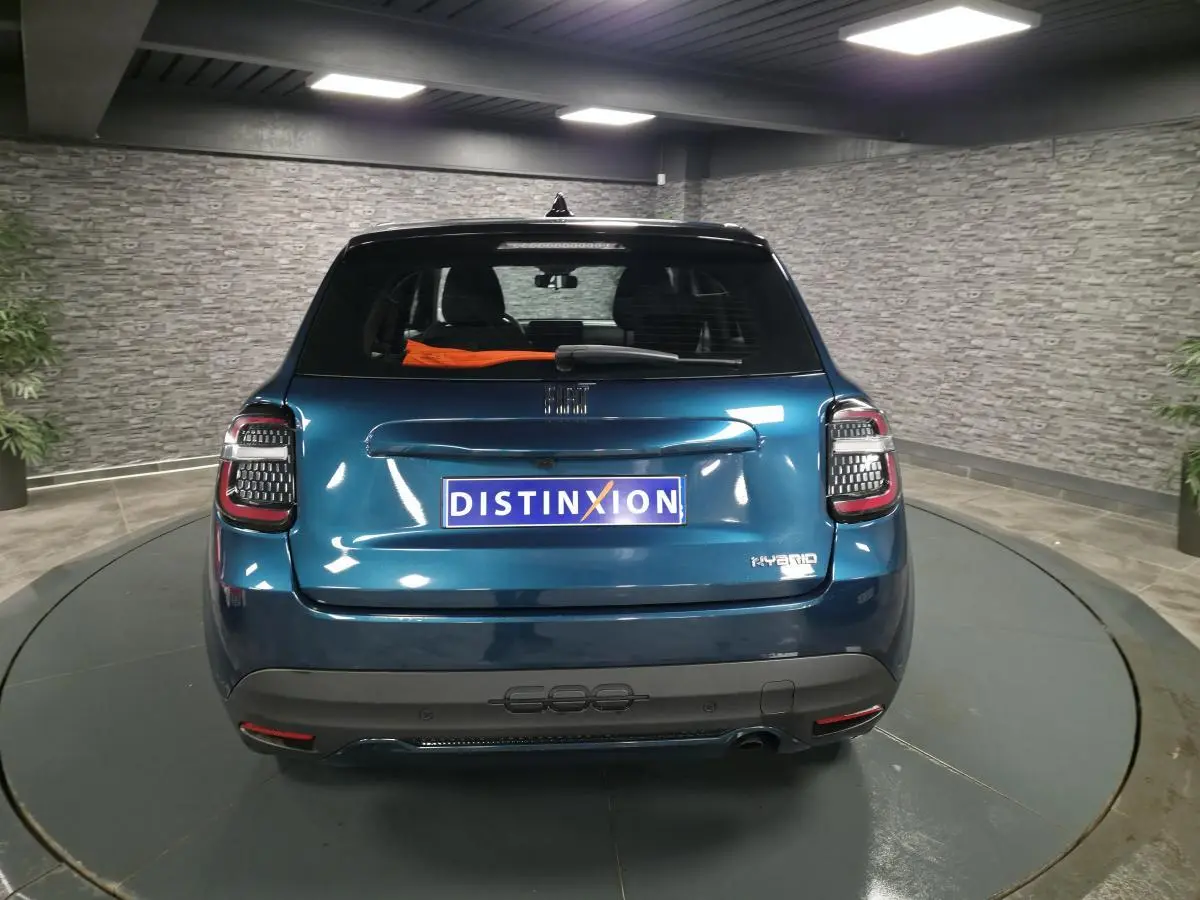 Vue arrière d'une FIAT 600 hybride bleue métallisée avec feux LED et logo Hybrid sur hayon dans un showroom.