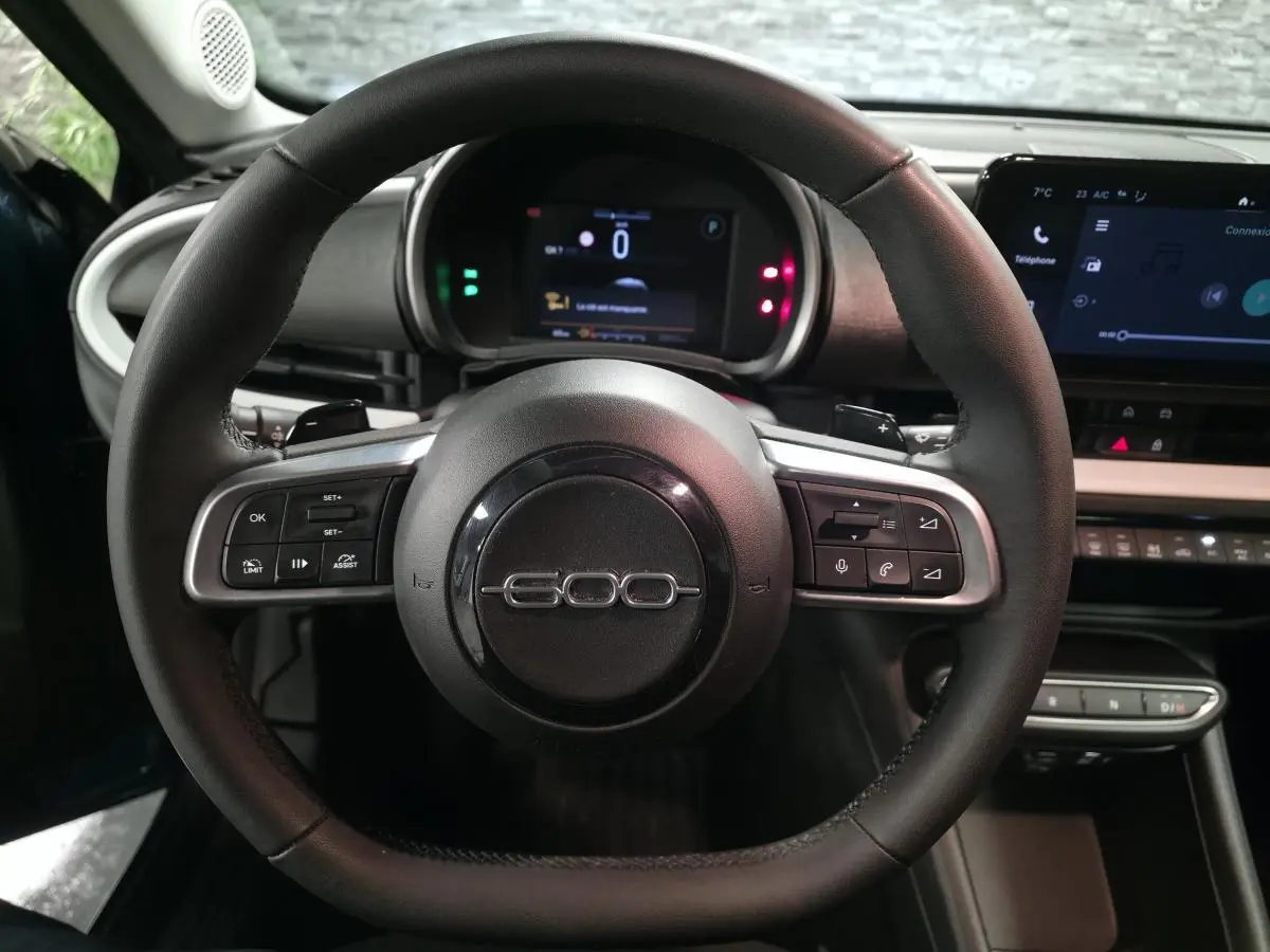 Vue intérieure centrée sur le volant noir de la Fiat 600 1.2 Hybrid 2024 avec tableau de bord numérique et écran tactile.