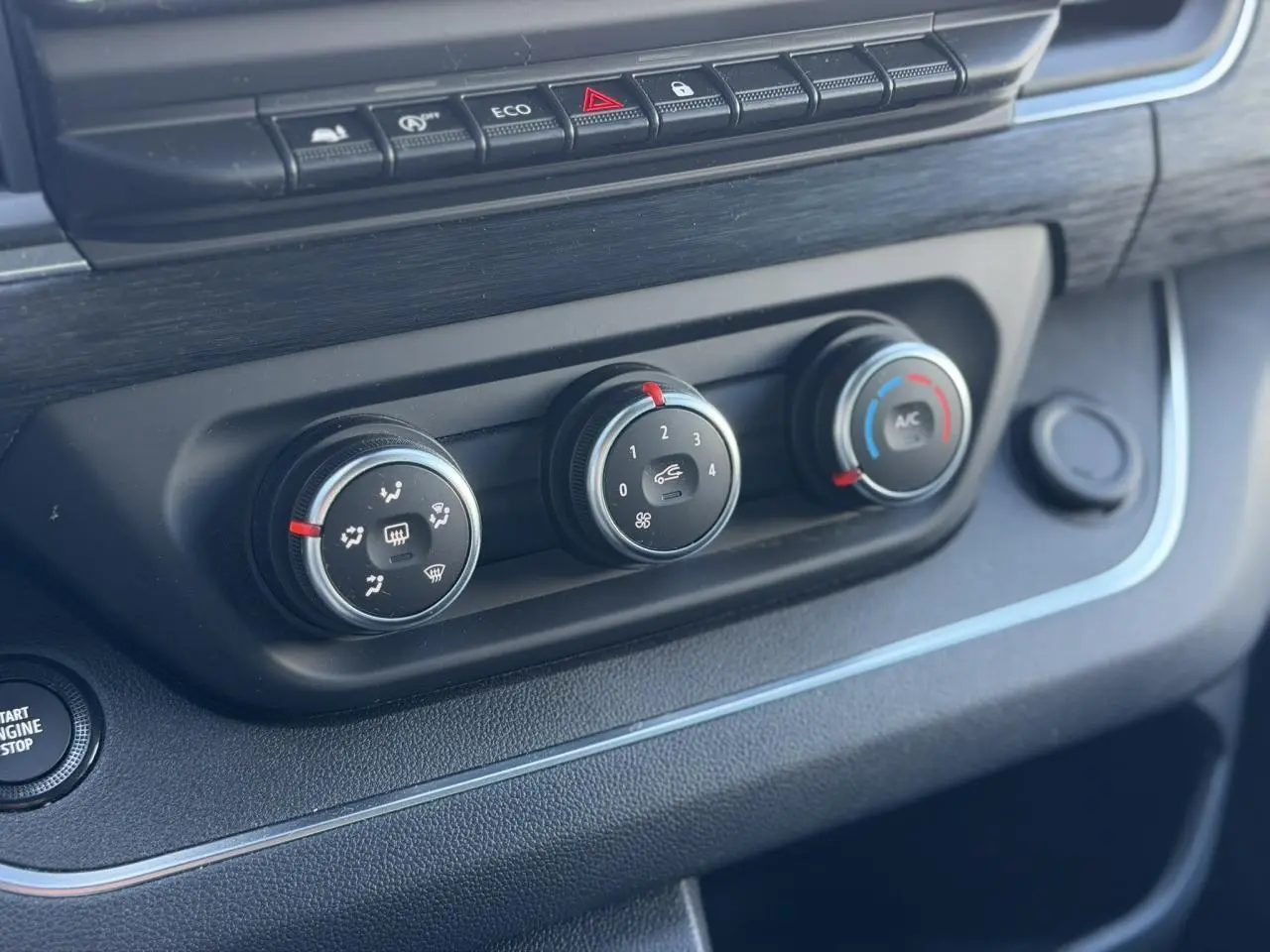 Vue rapprochée des commandes de climatisation et bouton start/stop du Nissan Primastar Combi gris, intérieur noir.