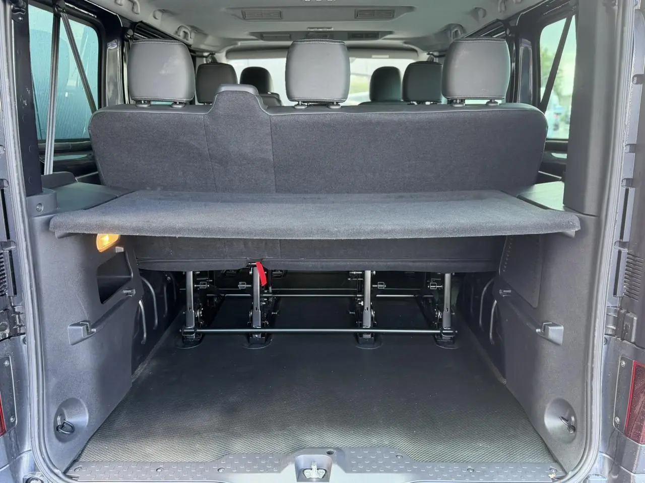 Vue arrière du Nissan Primastar Combi gris Comète montrant le hayon ouvert et l’espace de chargement avec cache-bagages.