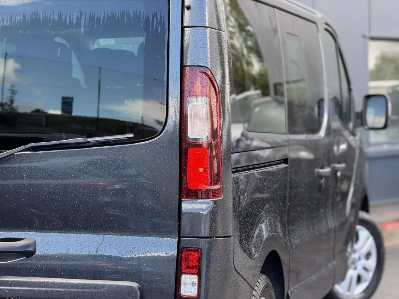 Vue arrière droite du Nissan Primastar Combi gris comète avec hayon vitré et jantes alliage 17 pouces.