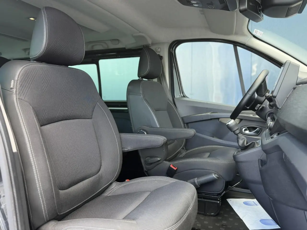 Vue intérieure côté droit du Nissan Primastar Combi 2025, sièges avant gris foncé avec accoudoirs et volant visible.