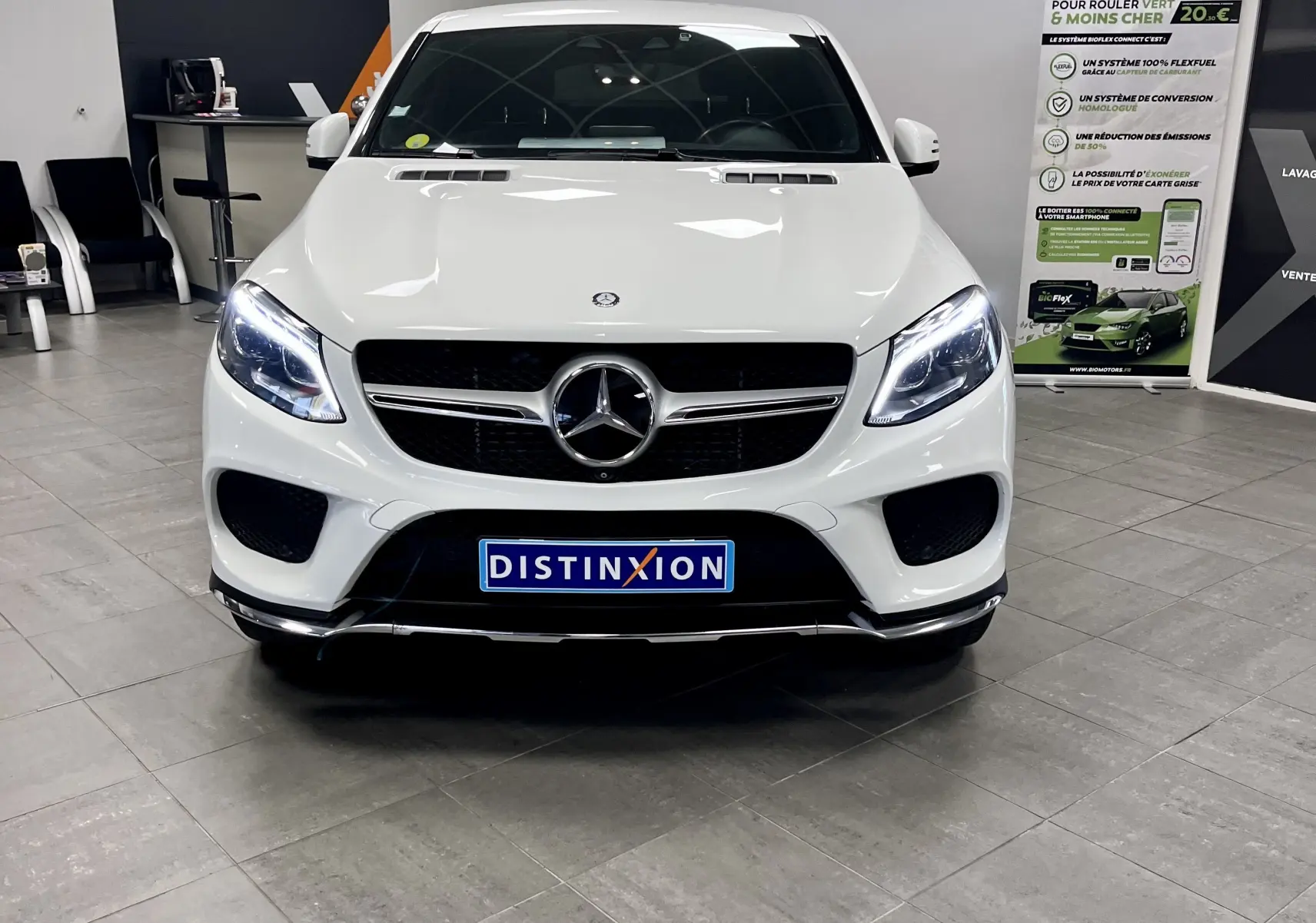 Vue avant d'une Mercedes GLE Coupe 350 d blanche avec phares allumés dans un showroom intérieur.