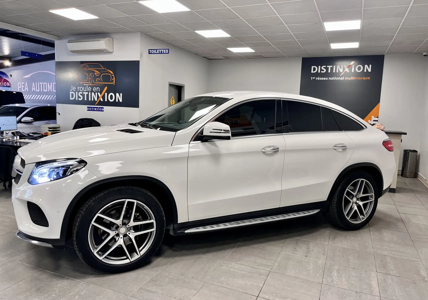 Vue de profil côté gauche d'un Mercedes GLE Coupe blanc 2016 avec jantes alliage et vitres teintées en showroom.