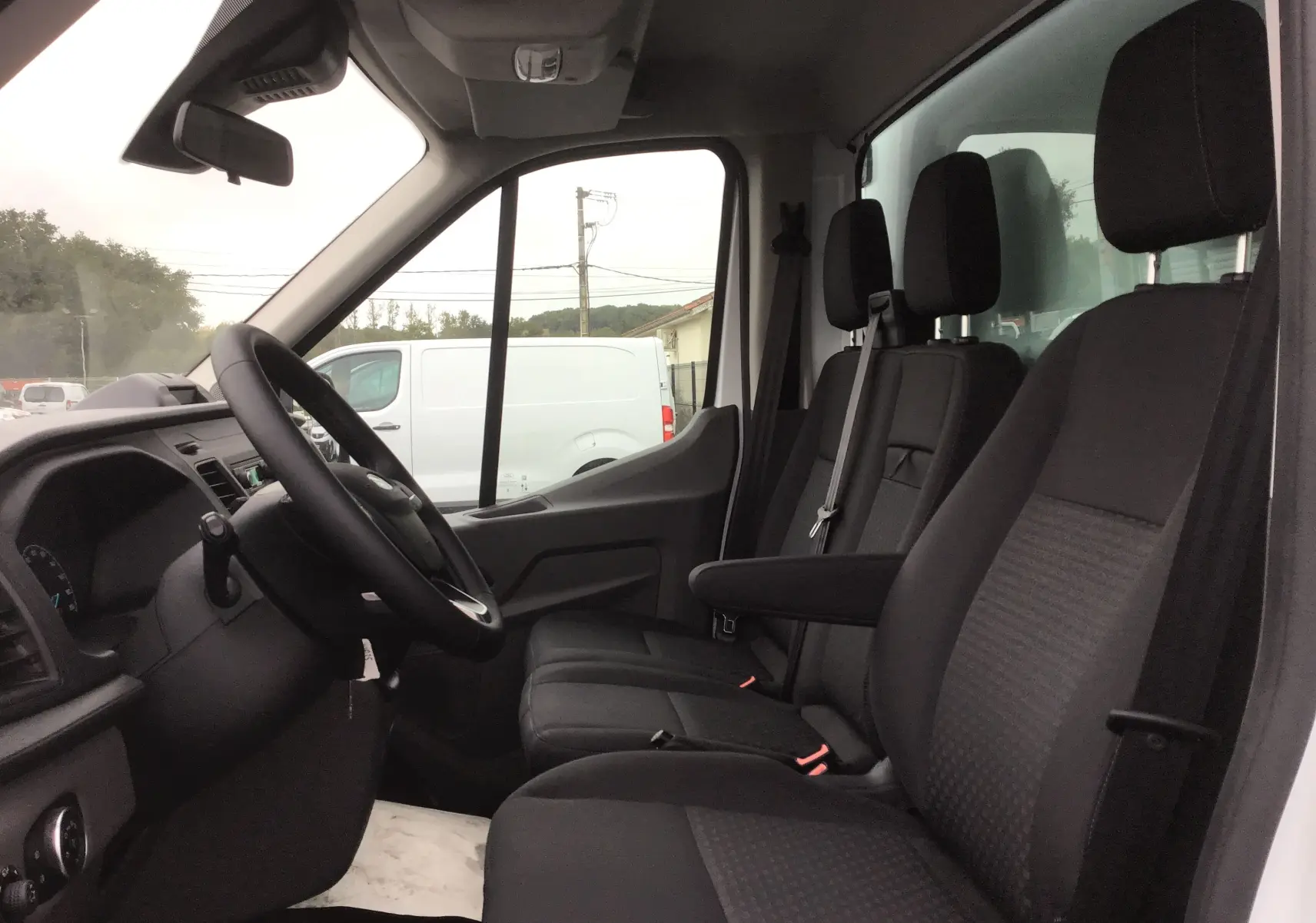Vue intérieure côté conducteur du Ford Transit Chassis Cabine blanc 2024, montrant les sièges noirs et le tableau de bord.