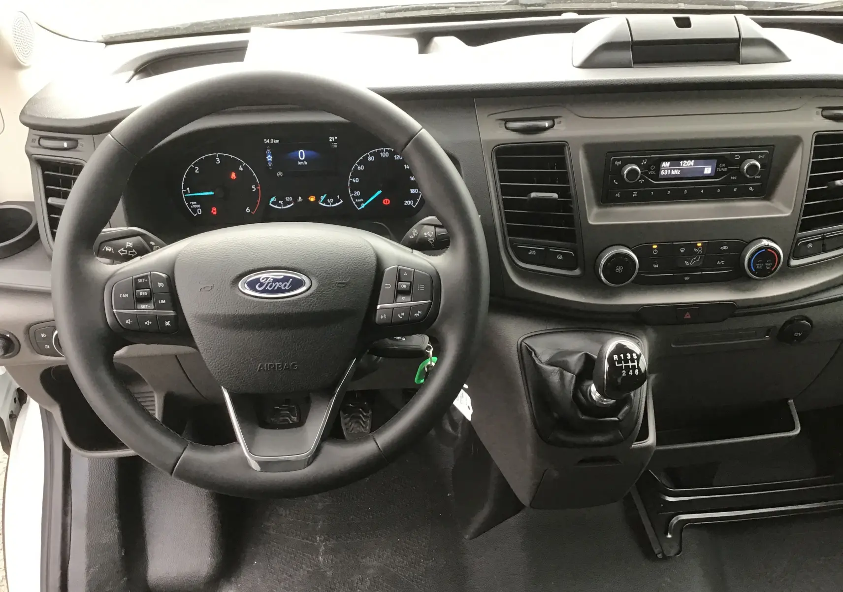 Vue intérieure du poste de conduite du Ford Transit Châssis Cabine blanc, avec volant multifonction et levier de vitesse manuel.