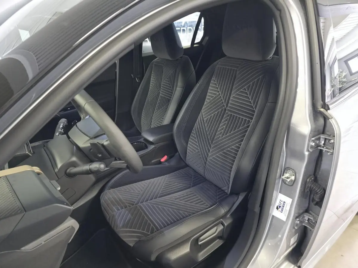 Vue intérieure côté conducteur de la Lancia Ypsilon 2025 gris, avec sièges velours gris à motifs géométriques.